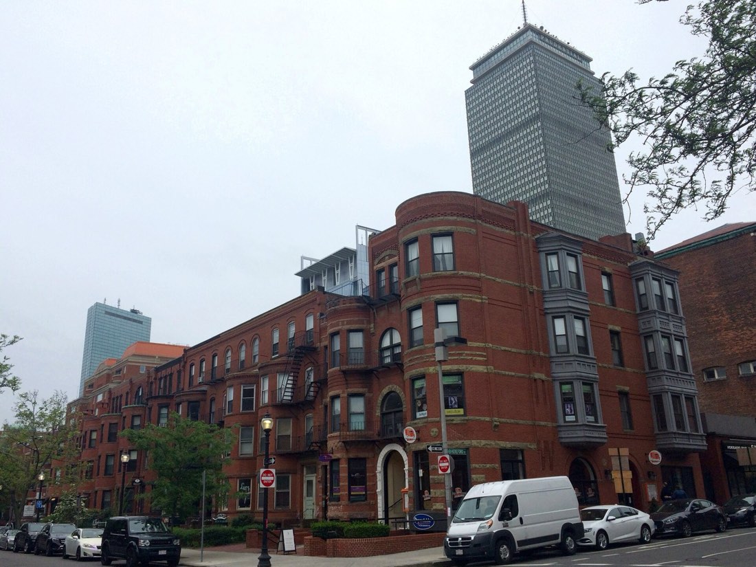 Brick rowhouses in Boston&rsquo;s Back Bay with the Prudential Tower rising behind them