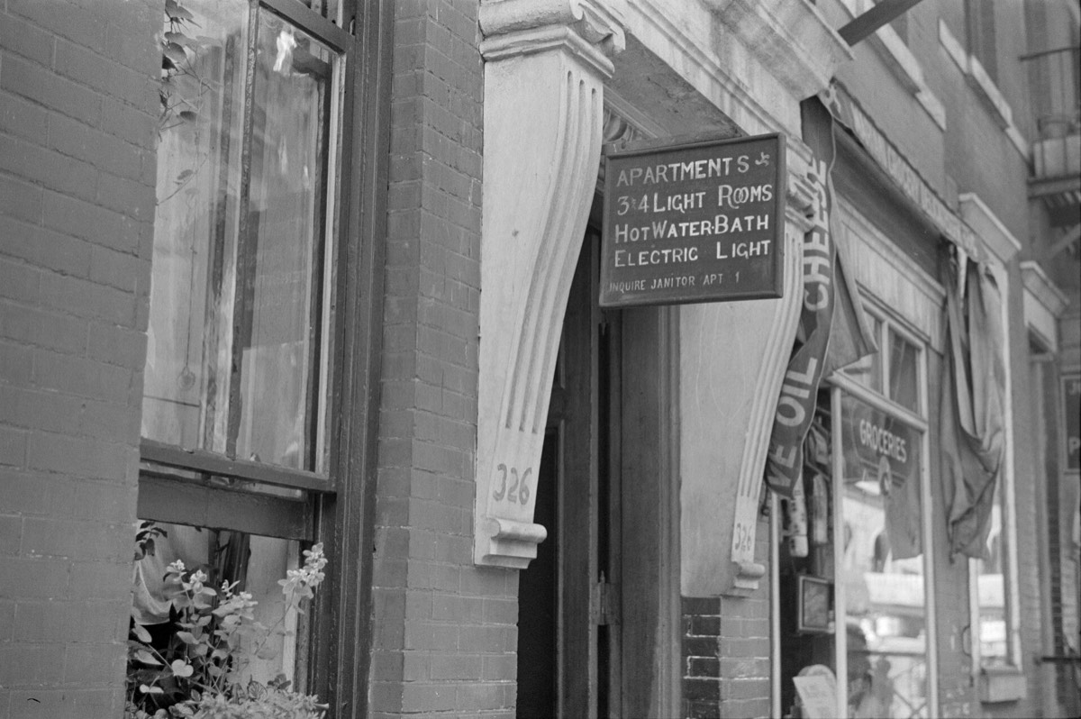 A hand-painted sign on a New York apartment building in 1938 advertising three and four light rooms, hot water bath and electric light